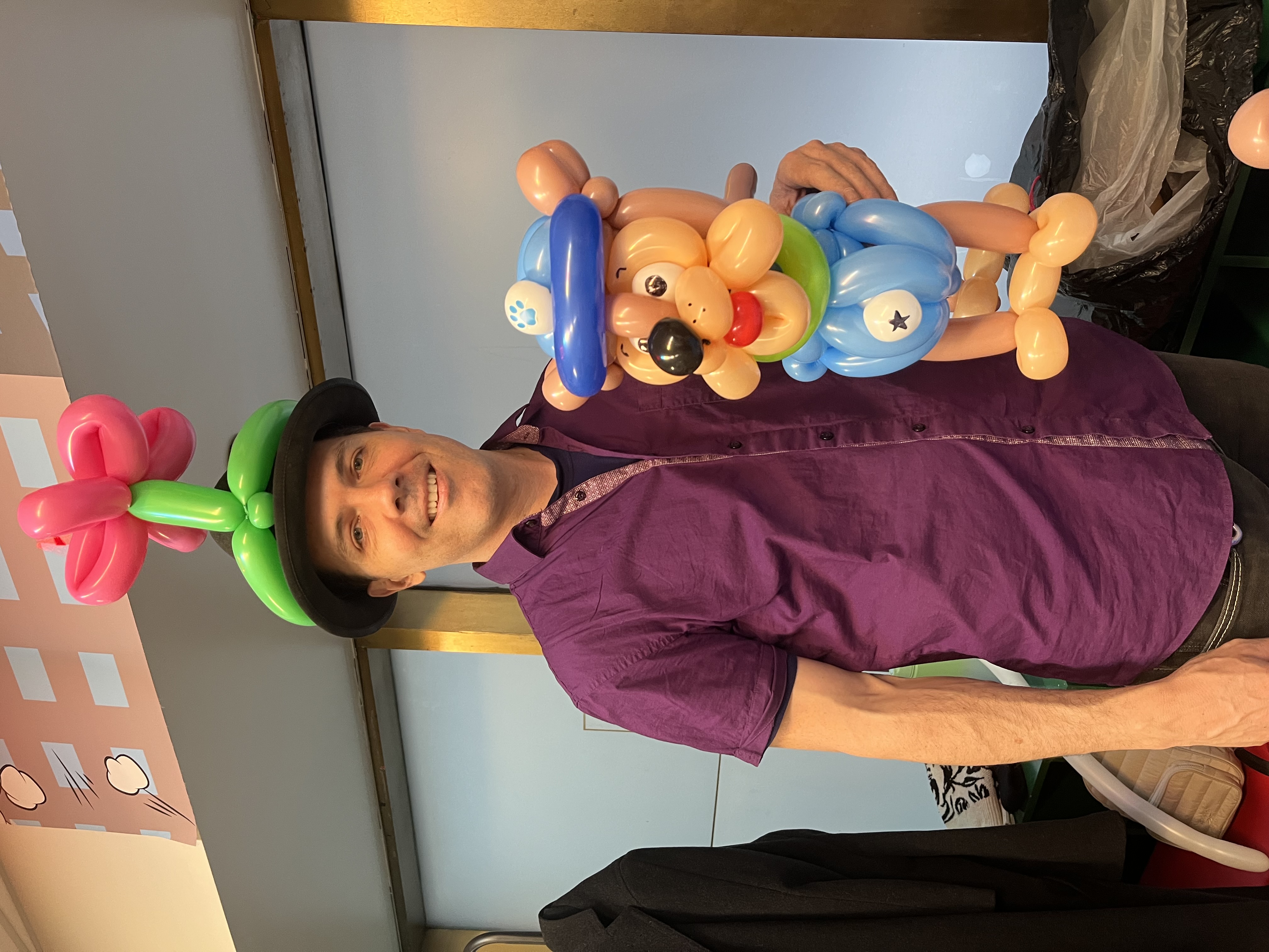 photo of a balloon artist wearing a flower balloon hat holding a balloon dog sculpture