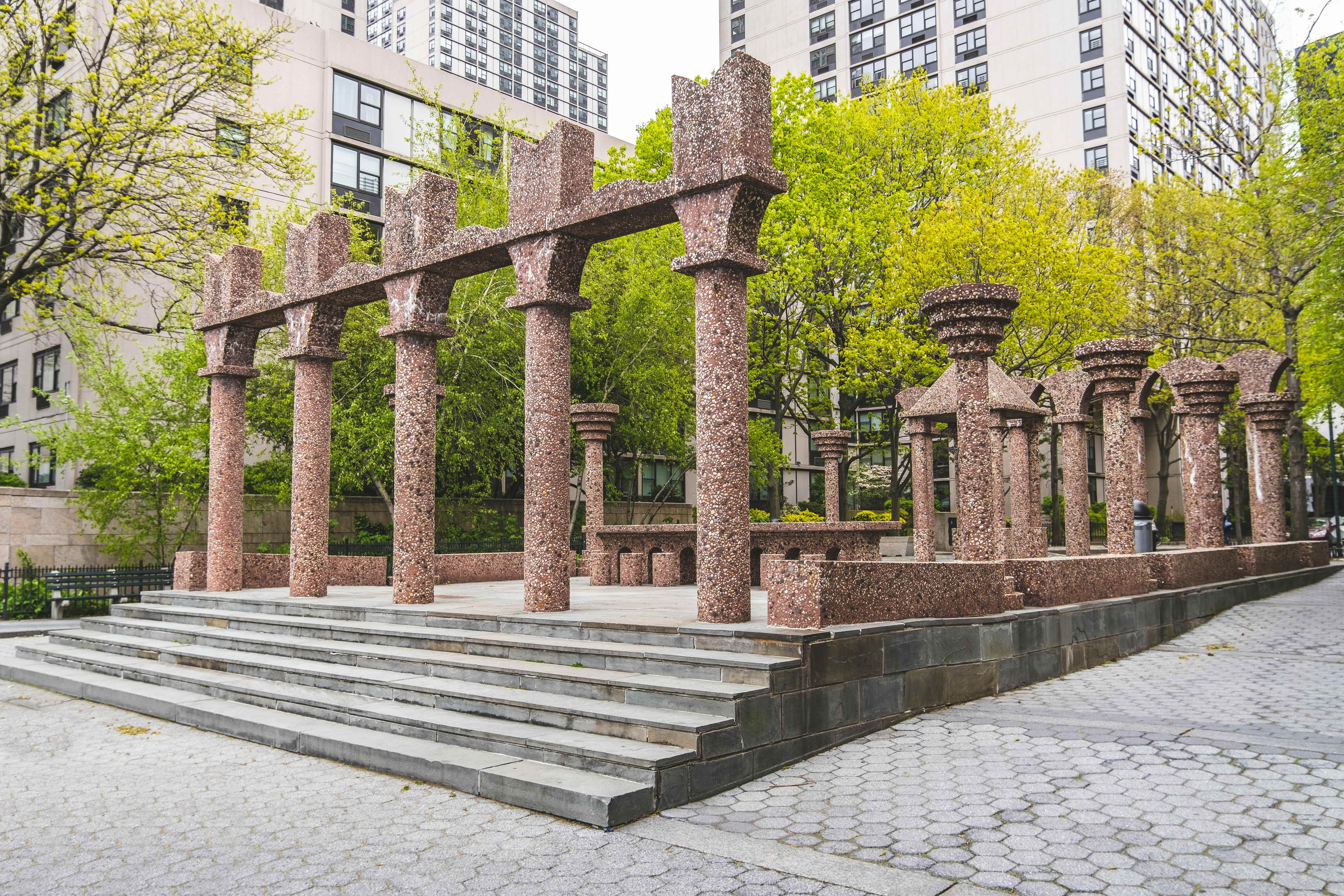 Battery Park City plaza with red granite colonnade sculpture surrounded by trees and residential towers
