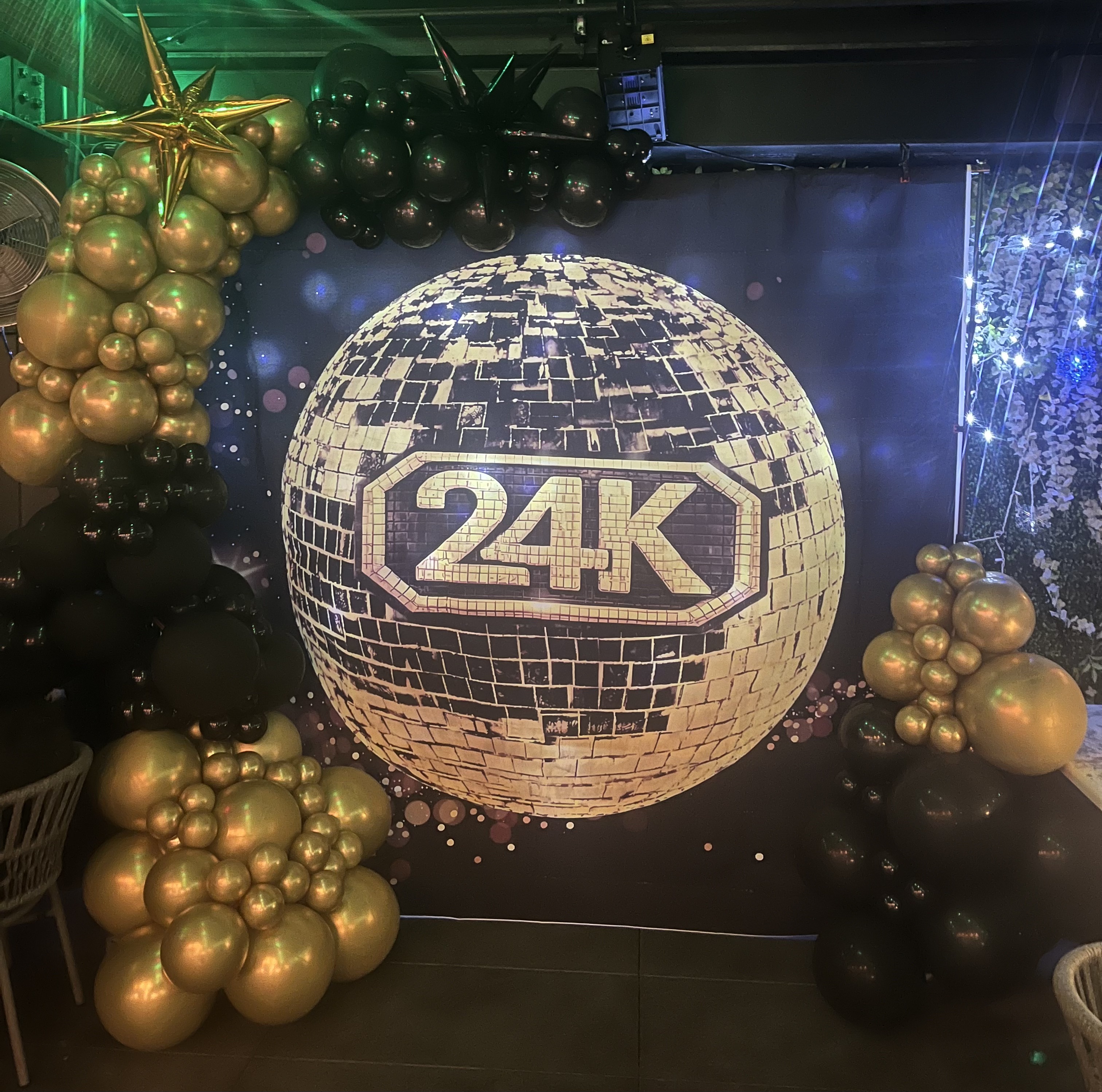 Gold and black balloon installation framing a 24K disco ball backdrop with star accents