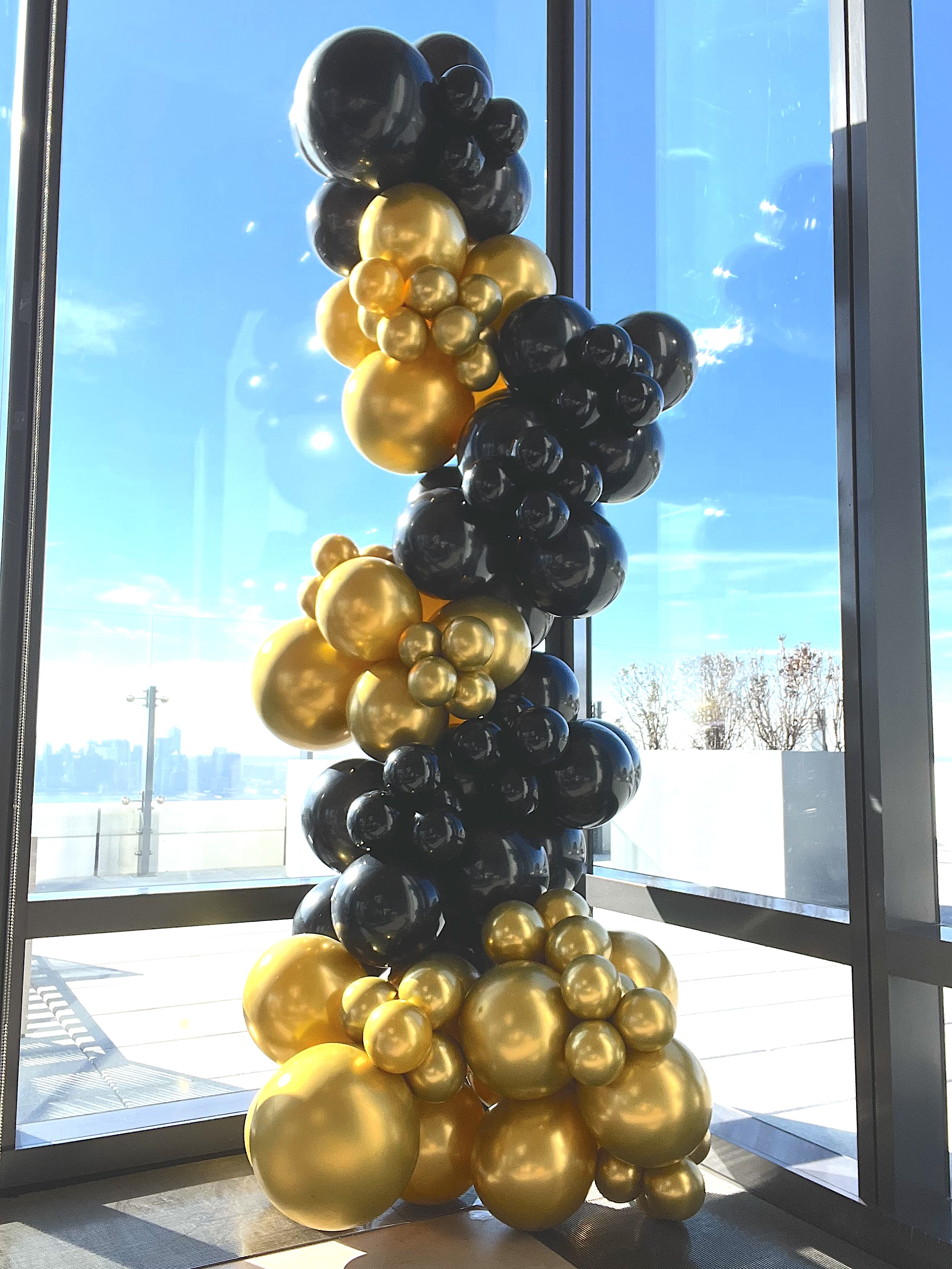 Elegant black and gold balloon column installation with NYC skyline view