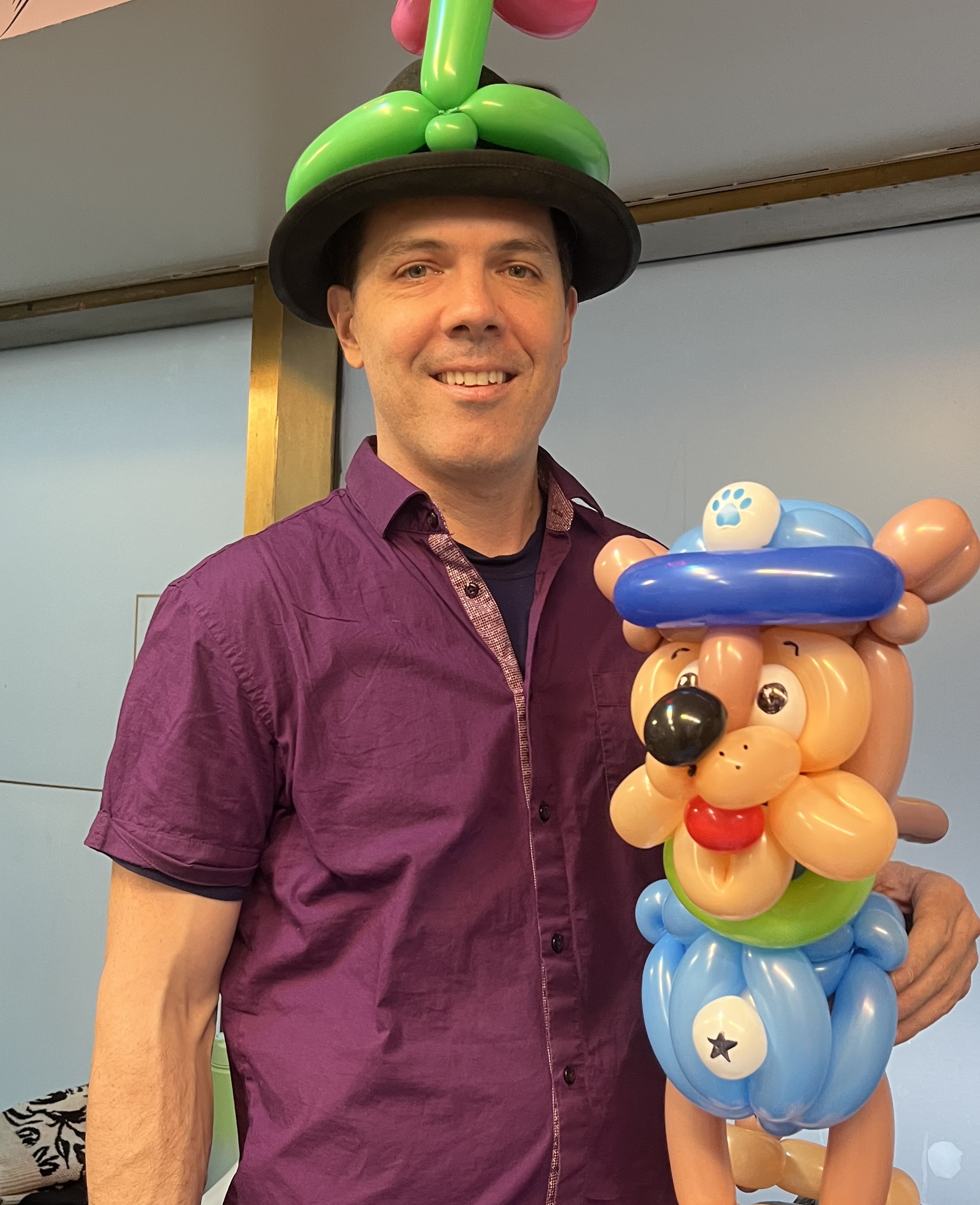 balloon artist wearing a green balloon hat and holding an elaborate balloon dog sculpture