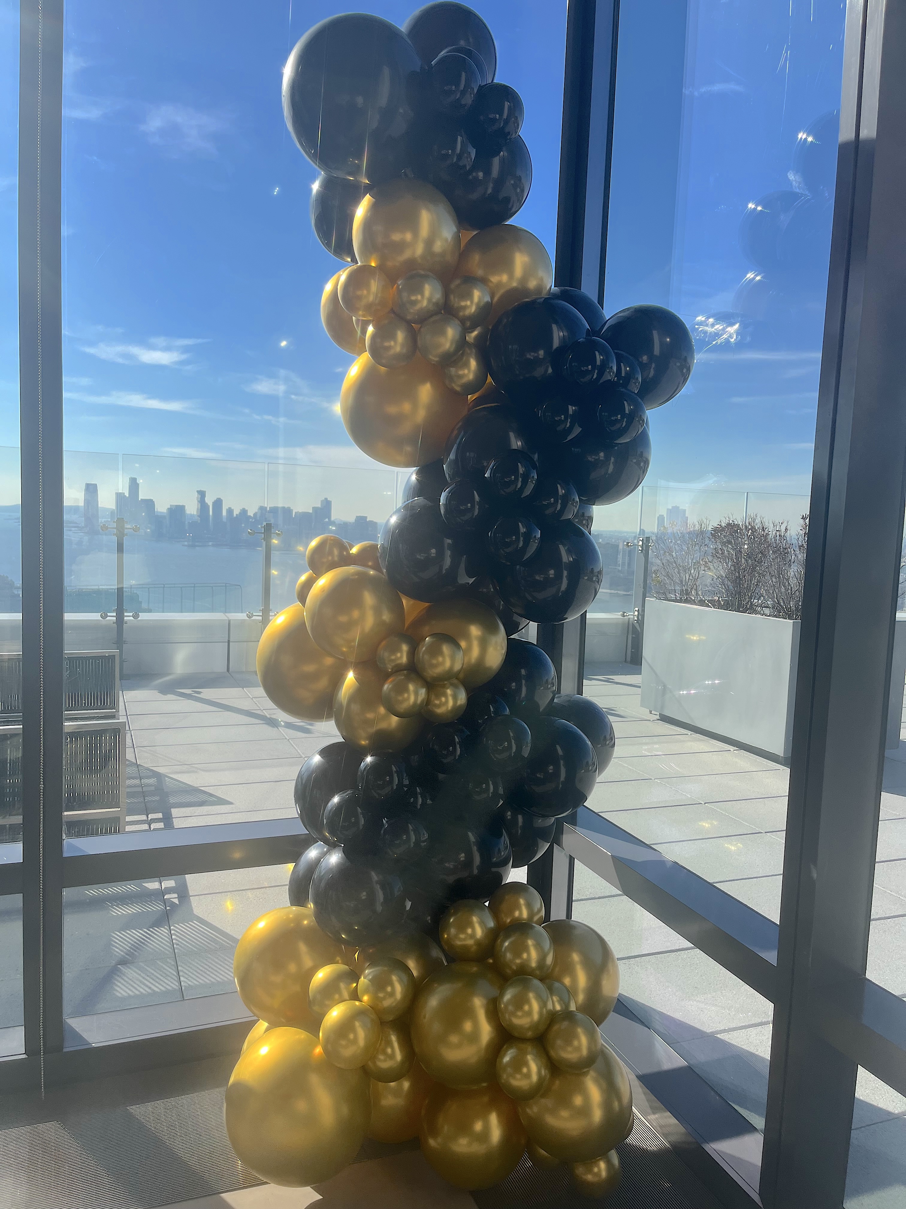 Elegant black and gold balloon column installation with NYC skyline view